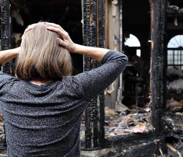 A woman with her back turned, both hands on her head, frightened to see her house damaged by fire.